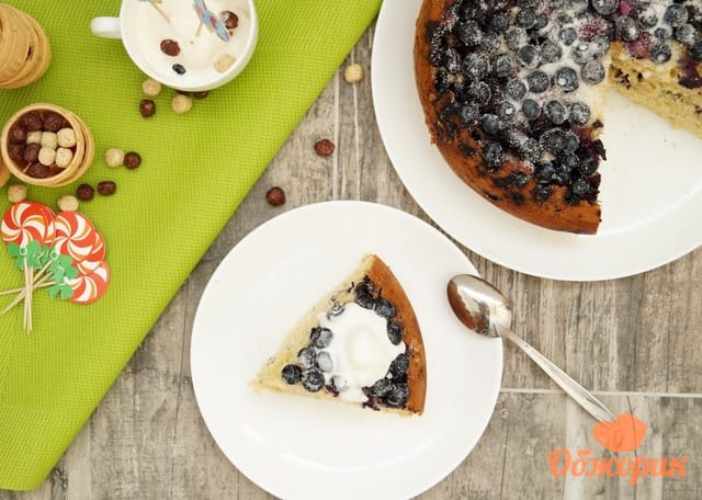 A blueberry cake with berries on top, one slice cut and lifted out
